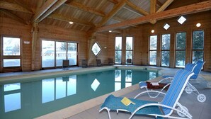 An indoor swimming pool with clear glass walls, wooden beams, and lounge chairs. - Spacious Alpine Chalet (Le Devoluy)