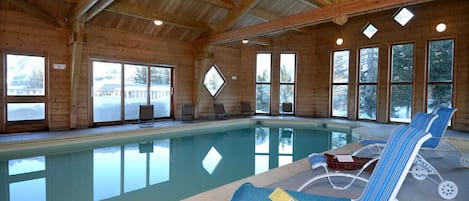 Une piscine intérieure avec des parois en verre transparent, des poutres en bois et des chaises longues.