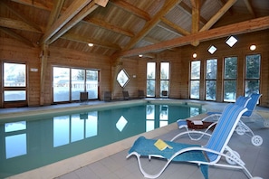 Ein überdachter Pool mit großen Glaswänden, Holzbalken und Liegestühlen.