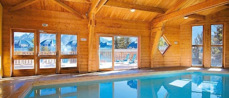 Un interior de madera con piscina, ventanas amplias y vistas al exterior.