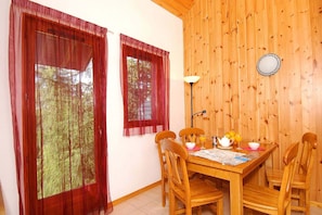 A dining area with a wooden table, chairs, and a window with red curtains. - Spacious Alpine Chalet (Le Devoluy)