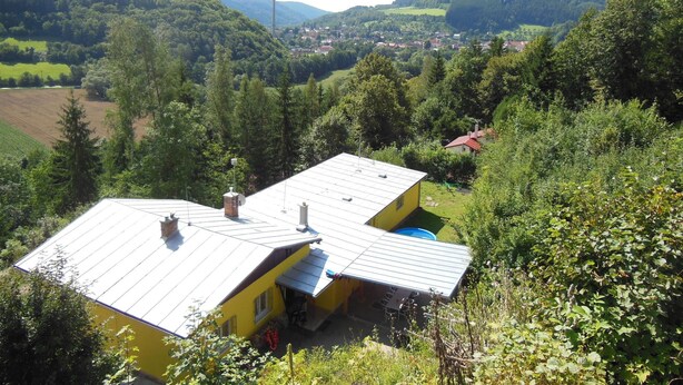 A yellow house with a metal roof, surrounded by lush greenery and hills in the background. - Child-friendly holiday home in Moravia with a beautiful location and view (Nedvedice)