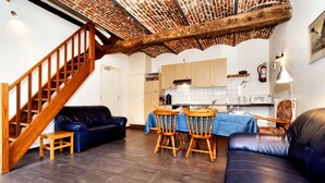 Una sala de estar con una escalera, un comedor con mesa y sillas, y una cocina con armarios y electrodomésticos.