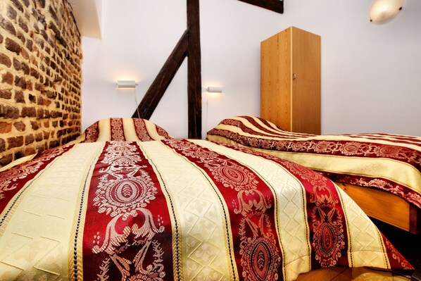 A room with a brick wall, wooden beams, and a bed with patterned bedding. - Nice apartments in a monumental square farm. (Richelle)