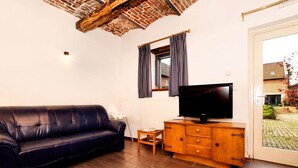 Una sala de estar con un sofá de cuero oscuro, un mueble de madera con un televisor de pantalla plana, una mesita de madera y una ventana con cortinas a cuadros.