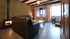 Un salón acogedor con una pared de piedra, una chimenea, un sofá de cuero, una mesa de centro de madera y un balcón con vistas.