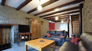 Una sala de estar acogedora con pared de piedra, vigas de madera, un sofá de cuero y una mesa de centro de madera.