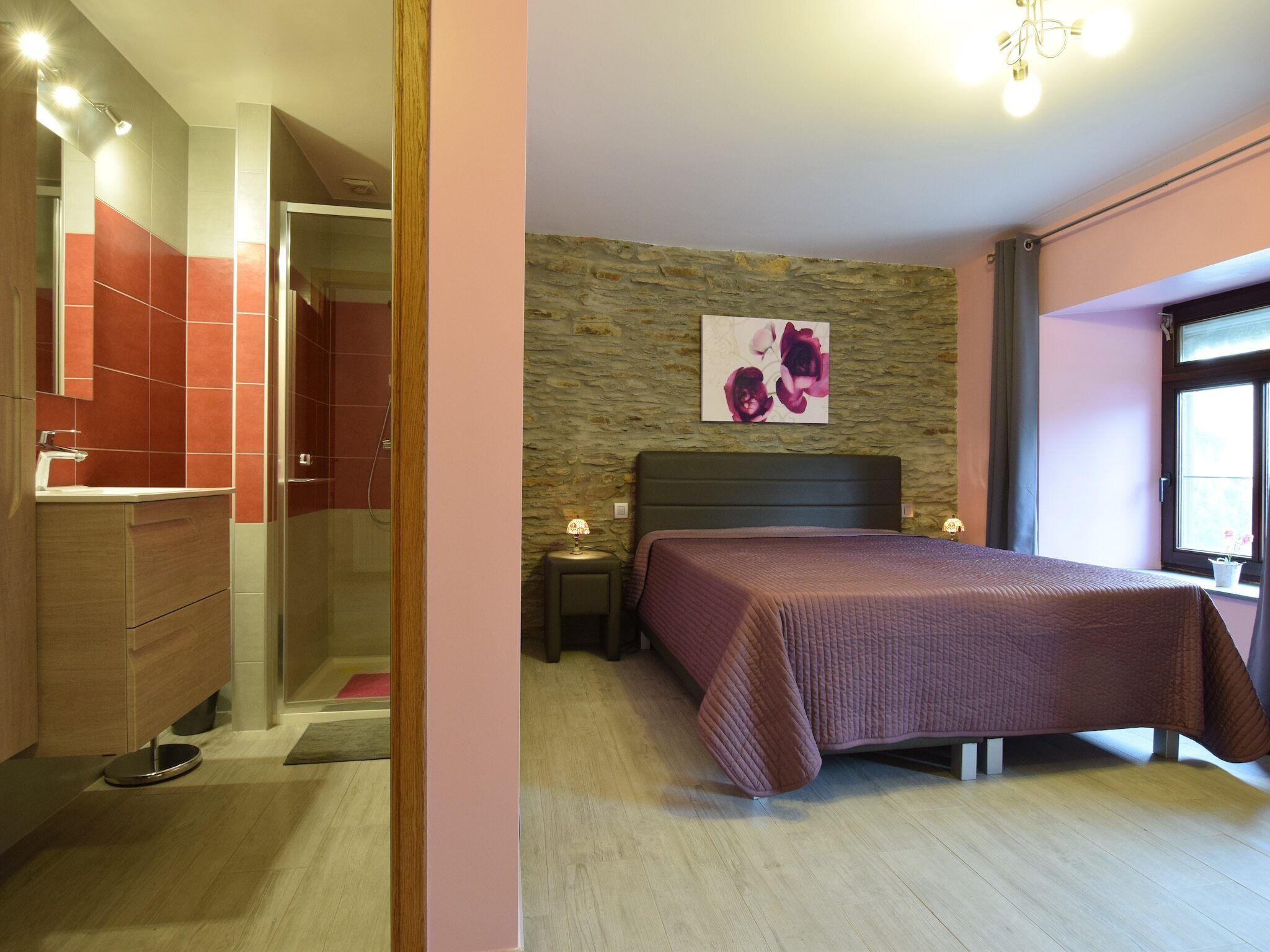 Un dormitorio con cama, mesita de noche, lámpara, pared de piedra y ventana.