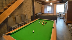 Una mesa de billar en una habitación con paredes de piedra, una escalera y un área de estar con sofá y sillones.