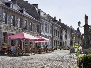 A cobblestone street with outdoor seating at a café, stone buildings, and a statue. - Limbourg Getaway with Charm (Limbourg)