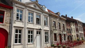 Eine Reihe historischer Gebäude mit Steinauffassungen und roten Akzenten, darunter eine gepflasterte Straße und Außenbereich mit Sitzgelegenheiten.