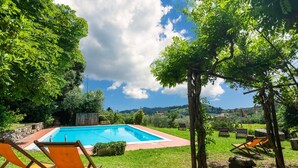 Piscina con dos sillas de descanso y una pérgola en un jardín exuberante.