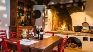 Una mesa de madera con sillas, un aparador con botellas y una chimenea encendida.