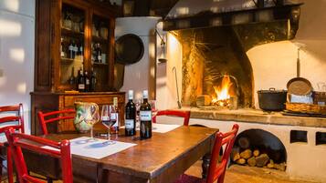 Un tavolo da pranzo in legno con sedie, un mobiletto con bottiglie e un camino acceso.