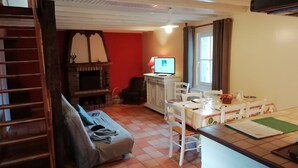 A cozy living room with a fireplace, a television, a dining table with chairs, and a sofa. - Holiday Home in Quend-Plage near Forest (Quend-Plage)