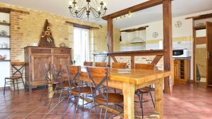 A rustic kitchen with a wooden dining table and chairs, a chandelier, and a brick wall.