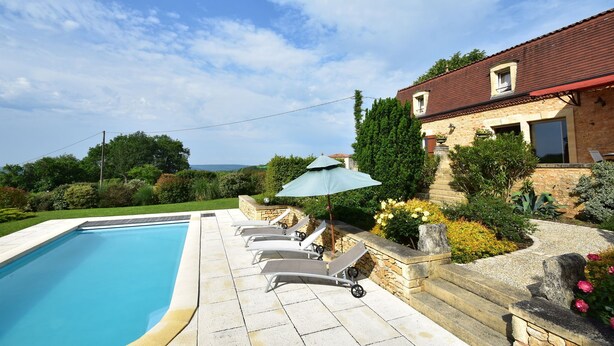 A swimming pool with lounge chairs and an umbrella, surrounded by a stone wall and greenery.