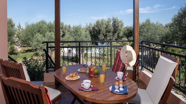 A wooden table set for breakfast with a view of olive trees and a pool.