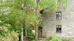 A stone building with a stone roof, surrounded by lush greenery and flowering shrubs. - Former farmhouse in a quiet village (Manhay-Freyneux)