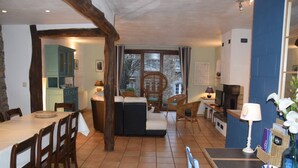 A spacious dining area with a long table and chairs, a cozy seating area with sofas and chairs, and a kitchen visible through an open doorway. - Former farmhouse in a quiet village (Manhay-Freyneux)