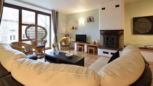 A living room with a sofa, wicker chairs, a TV, a fireplace, and a bookshelf. - Former farmhouse in a quiet village (Manhay-Freyneux)