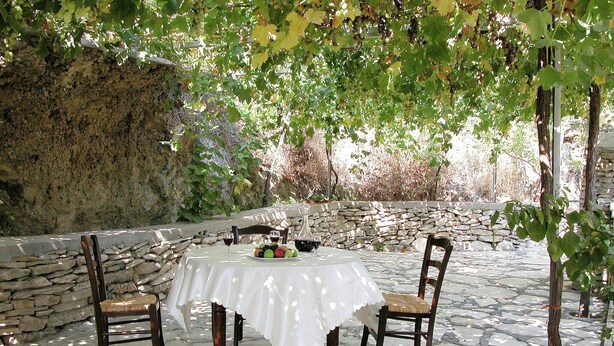 An outdoor patio with a stone table and chairs, surrounded by a stone wall and greenery. - Villa in Crete with Private Pool & Views (Malades)