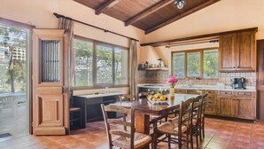 A spacious kitchen with wooden cabinets, a dining table with chairs, and large windows providing natural light. - Villa in Crete with Private Pool & Views (Malades)