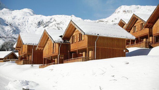 A wooden chalet-style hotel with multiple balconies, set against a snowy mountain backdrop.