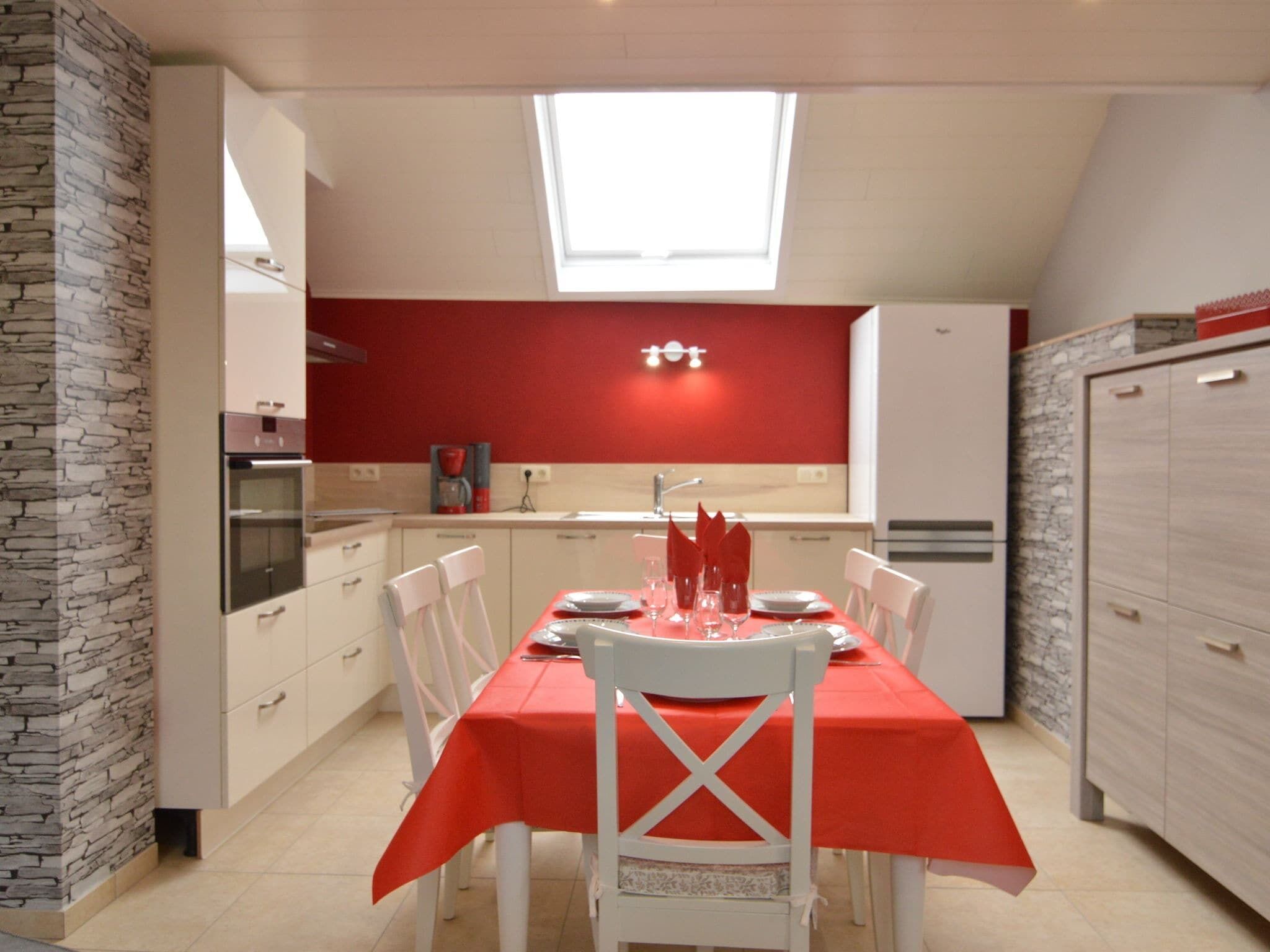 Cucina compatta con zona pranzo, caratterizzata da una parete rossa, mobili bianchi e un lucernario.