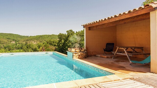 A swimming pool with a view of green hills, a covered patio area with a table and chairs, and a stone planter with plants. - Peaceful Villa in Calamane with Private Pool (Calamane)
