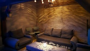 A cozy, dimly lit room with a cushioned seating area, a small table, and a unique ceiling light fixture.