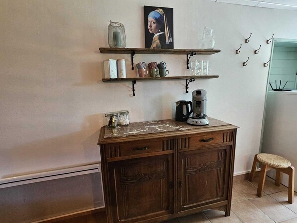 Una cocina con armarios de madera, cafetera y estantes con frascos y tazas.
