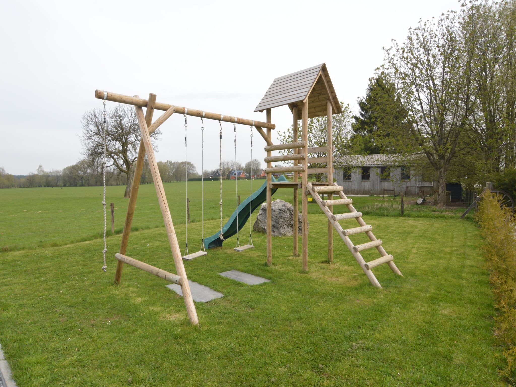 Une balançoire en bois avec un toboggan et un petit abri.