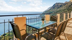 A balcony with a glass table and chairs overlooking a coastal view with a mountain in the background. - Studio in Ravdoucha with Sea View Balcony (RAVDOUCHA)