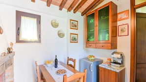 A compact kitchen with wooden cabinets, a refrigerator, a coffee machine, and a dining table with chairs.