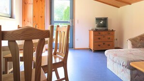 Une pièce avec un plafond en bois, un téléviseur posé sur une commode, un lit et une table à manger avec des chaises.
