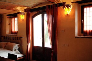 Une piĂšce avec un lit, une porte et deux fenĂȘtres avec des rideaux.