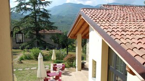 Une terrasse avec des tables et des chaises rouges, un mur jaune et une vue sur les montagnes.