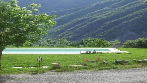 Un paysage naturel comprenant une zone herbeuse, une piscine et une vue sur des collines.