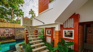 A modern outdoor staircase leading to a pool area, surrounded by lush greenery and a mix of brick and stone walls.