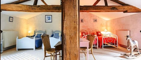 A room with a high ceiling, exposed wooden beams, two beds with different bedding, a dining table with chairs, and a small decorative horse figure.