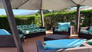 Une terrasse extérieure aménagée avec des meubles en osier, un espace abrité et une vue sur la verdure et les montagnes.