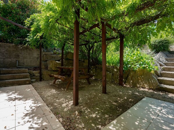 Un mur de pierre, une pergola en bois et une table de pique-nique dans un espace aménagé en jardin.