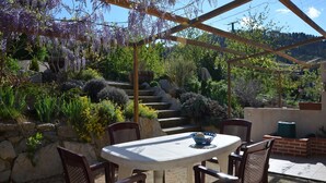 An outdoor patio with a round table and four chairs, surrounded by a pergola with purple flowering vines.