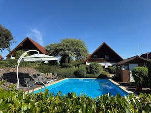 Una piscina con sillas de descanso y sombrillas, rodeada de casas con tejados inclinados.