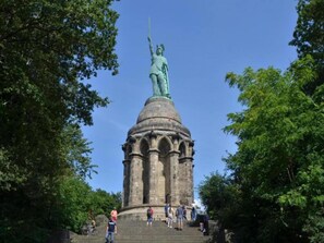 A large statue on a pedestal with steps leading up to it, surrounded by trees.