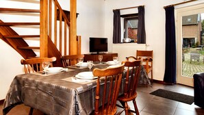 Un coin repas avec une table dressée pour quatre personnes, des chaises en bois, un téléviseur et une fenêtre avec des rideaux.