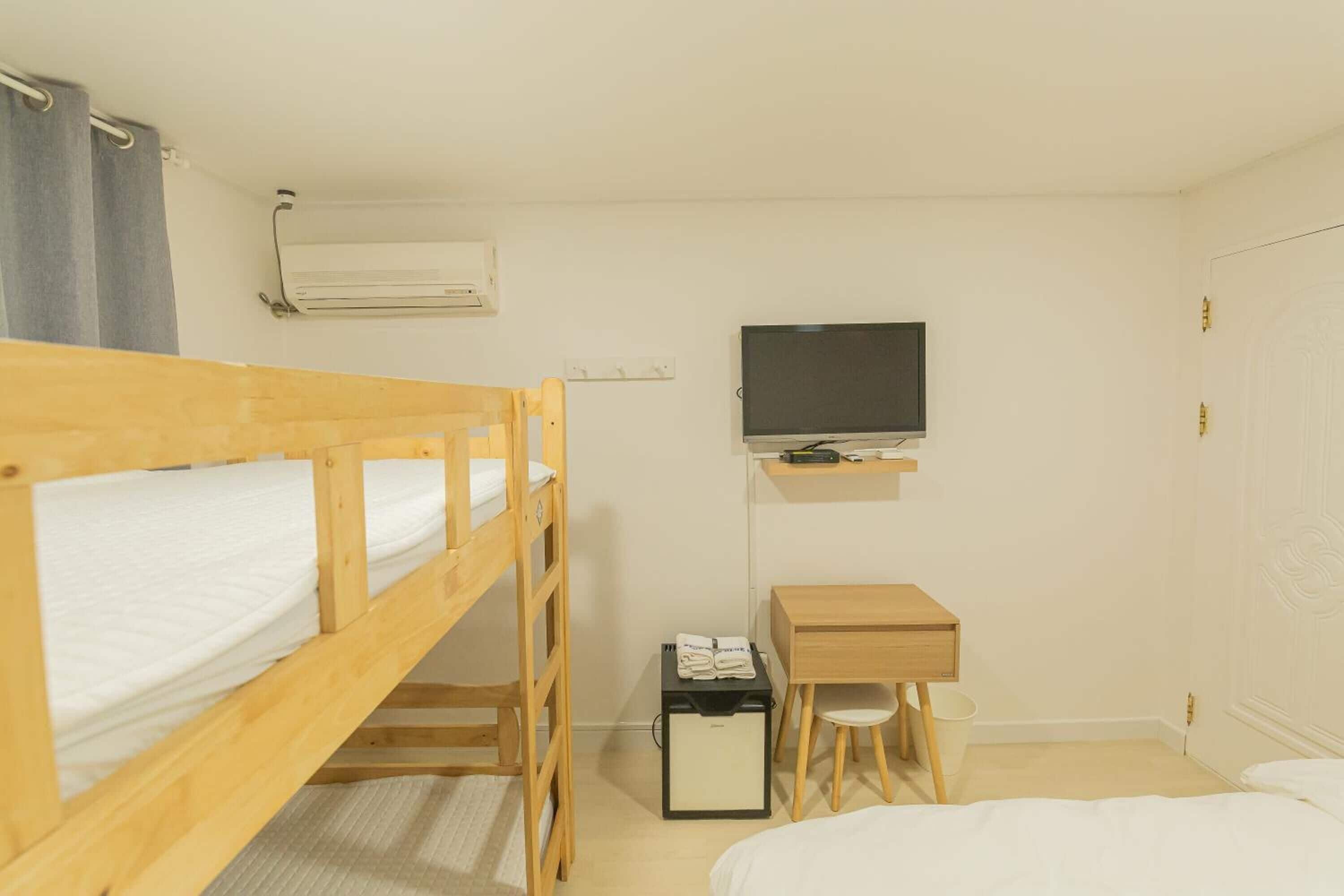 Een kleine, schone kamer met een stapelbed, een bureau, een stoel, een televisie en een kledingkast.