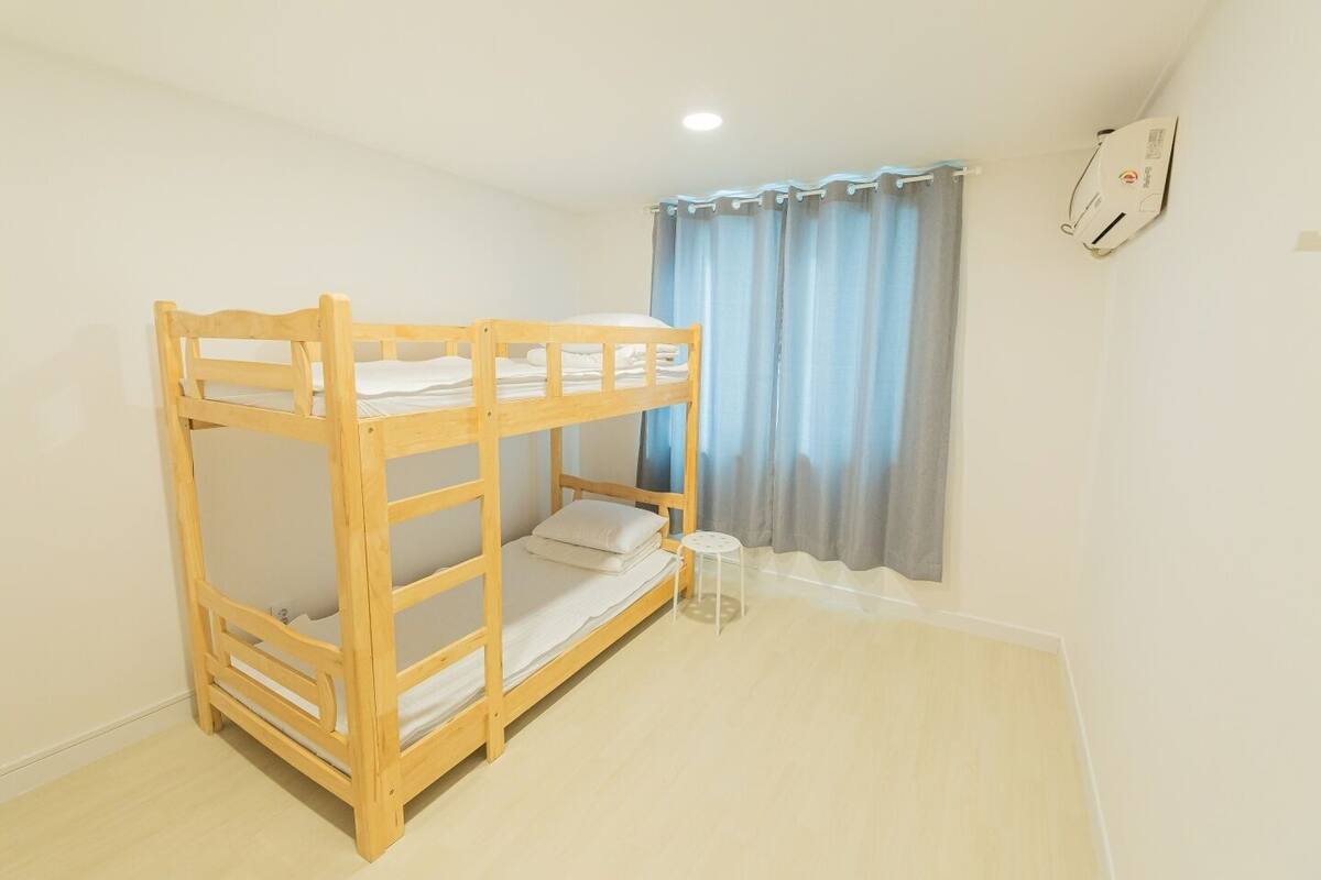 Una cama litera en una habitación con una mesita pequeña y una cortina.