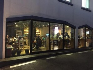 Un restaurant doté de grandes baies vitrées, d’une terrasse et d’un intérieur visible avec des tables et des chaises.